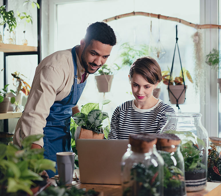 A woman with a laptop computer shares information with the young owner of an indoor plant store