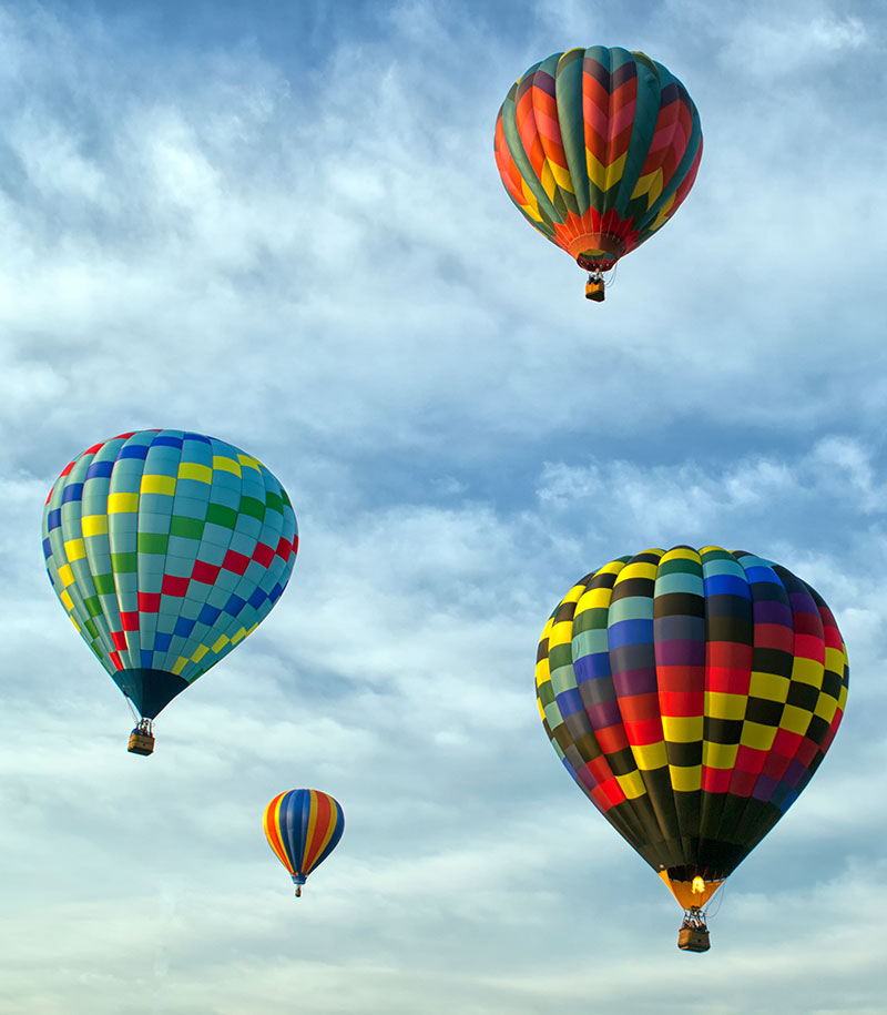 Four brightly colored hot air balloons fly in a blue sky at a large event