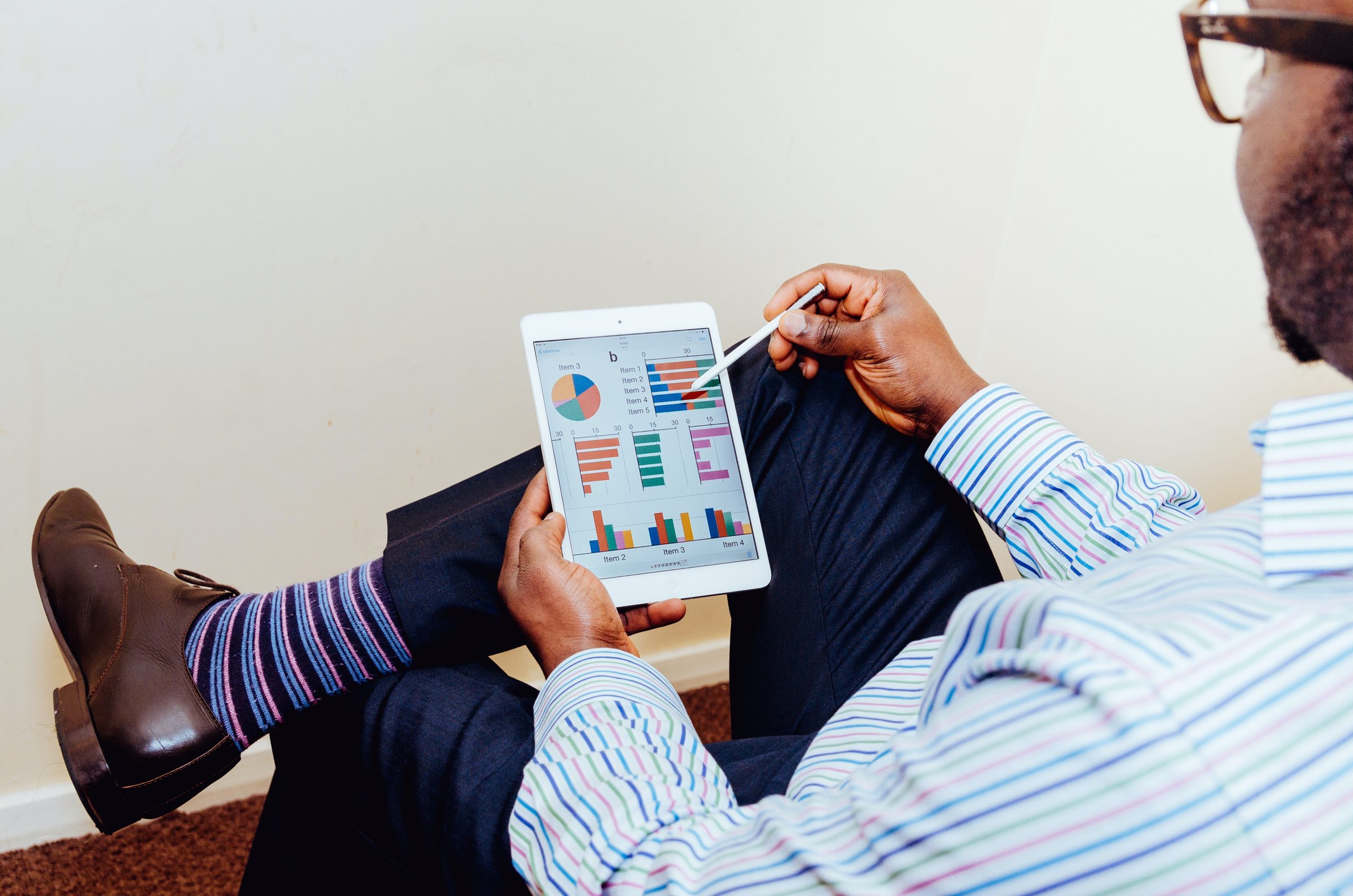 A man sits with one leg crossed over the other while looking at a data dashboard on a tablet computer