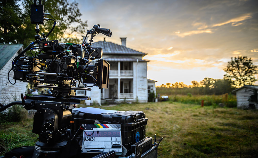 A digital movie camera is set up in front of a two story house in a rural community