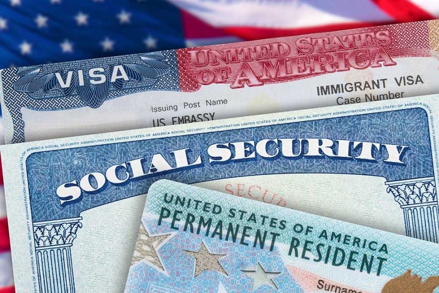 A US social security hard, work Visa, and immigration green card are seen on top of an American flag