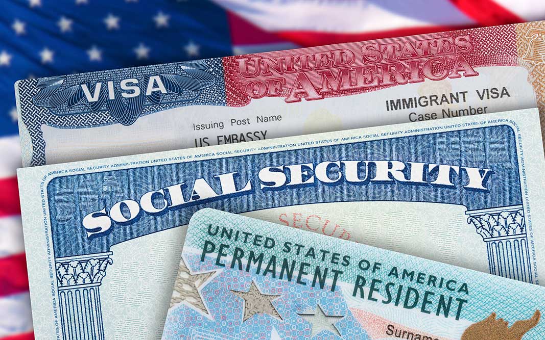 A US social security card, immigrant Visa, and permanent resident "green card" are seen in front of an American flag