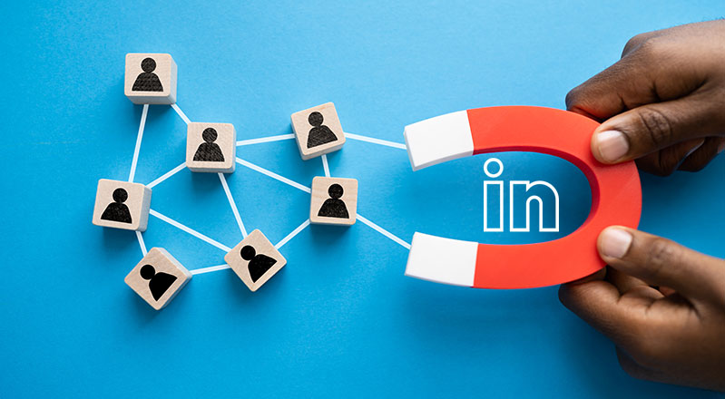 Hands hold a magnet with the LinkedIn logo on it that is attached to small wooden blocks with non-gender specific avatars on them