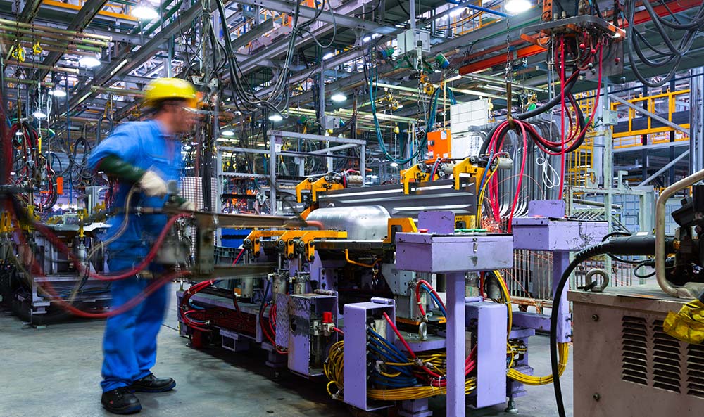 A person wearing a jumpsuit and hard hat uses heavy equipment in a manufacturing plant