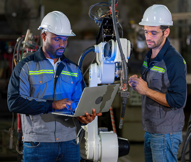 Two Advanced Manufacturing workers program a robotic arm using a laptop computer