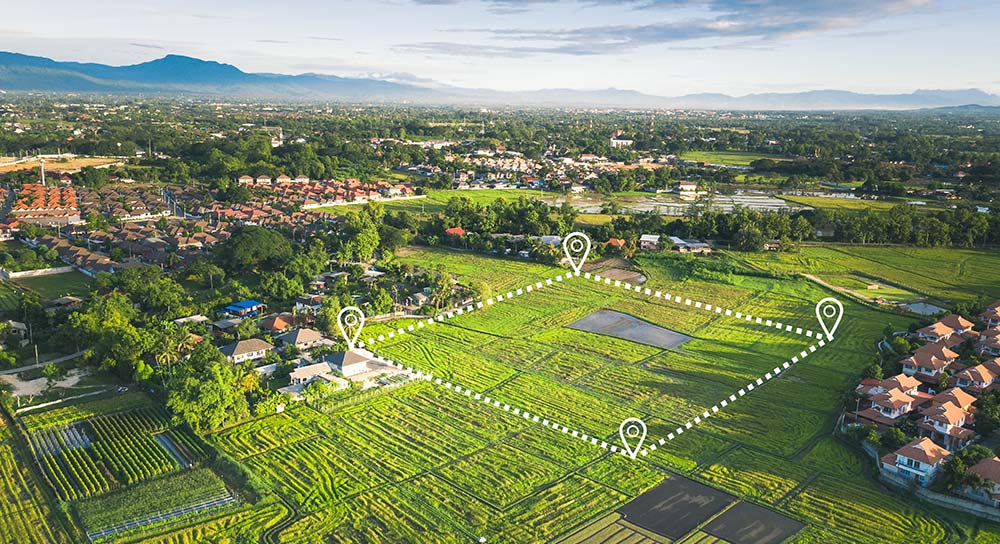 An aerial image shows a dotted line square over a large open grassy field with map pins in each corner indicating the planned location of a new real estate development