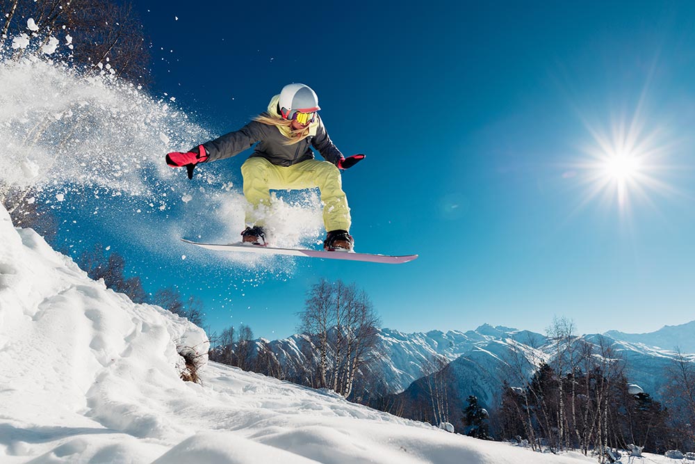 A snowboarder flies through the air surrounded by white snow and a blue sky