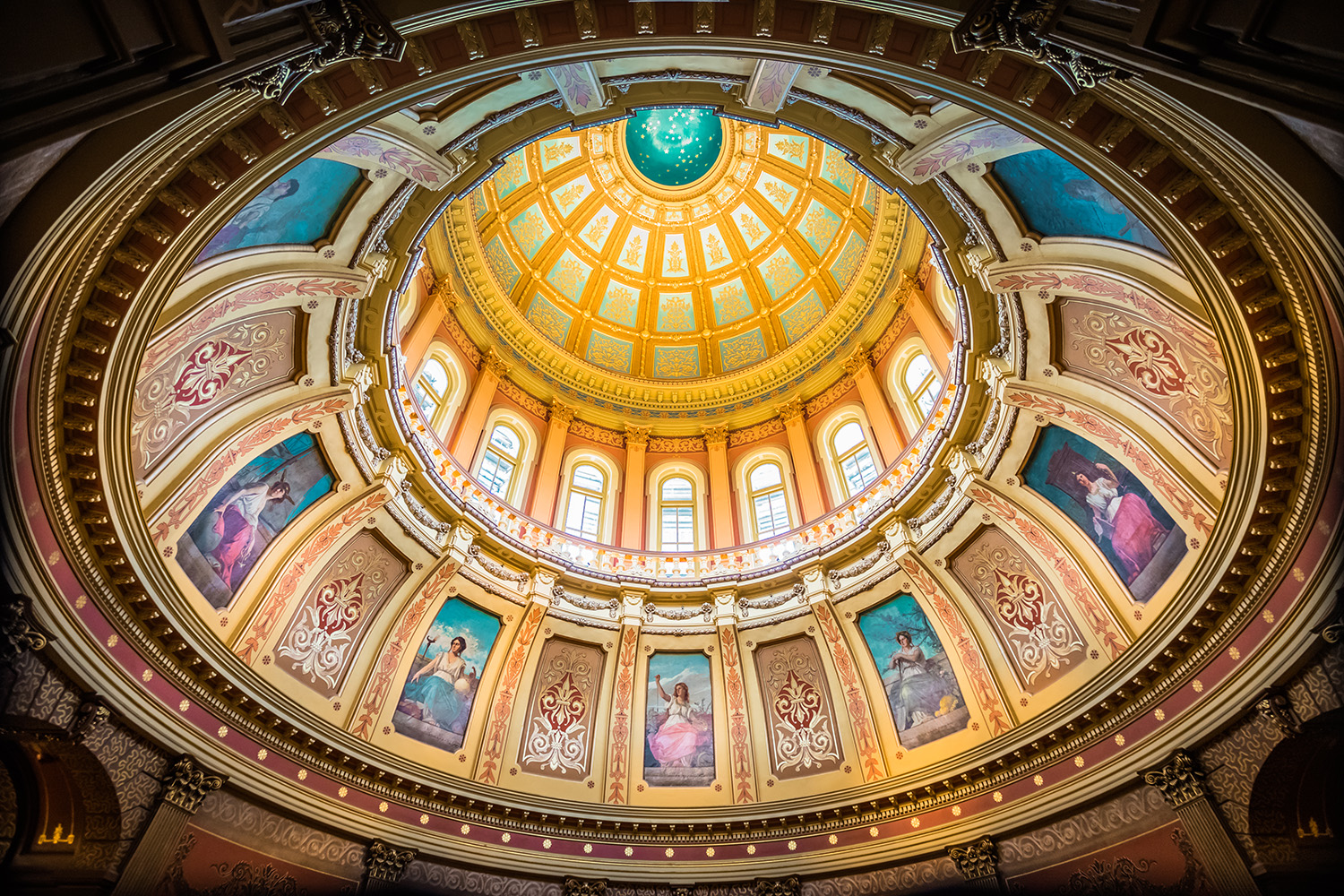 The colorful interior of the Michigan State Capitol dome features eight "allegories," figures of women representing various aspects of Michigan, including arts, agriculture, law, science, justice, industry, commerce, and education, painted by Italian artist Tommaso Juglaris just below the dome's oculus. 