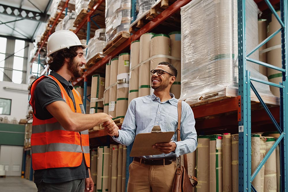 An economic developer greets a supervisor in an orange vest and hard hat at a local business