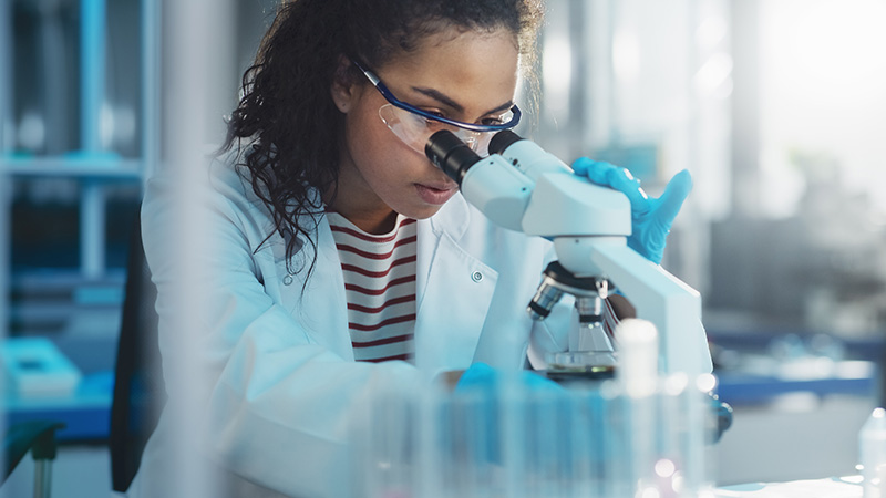 A woman looks into a microscope in a lab