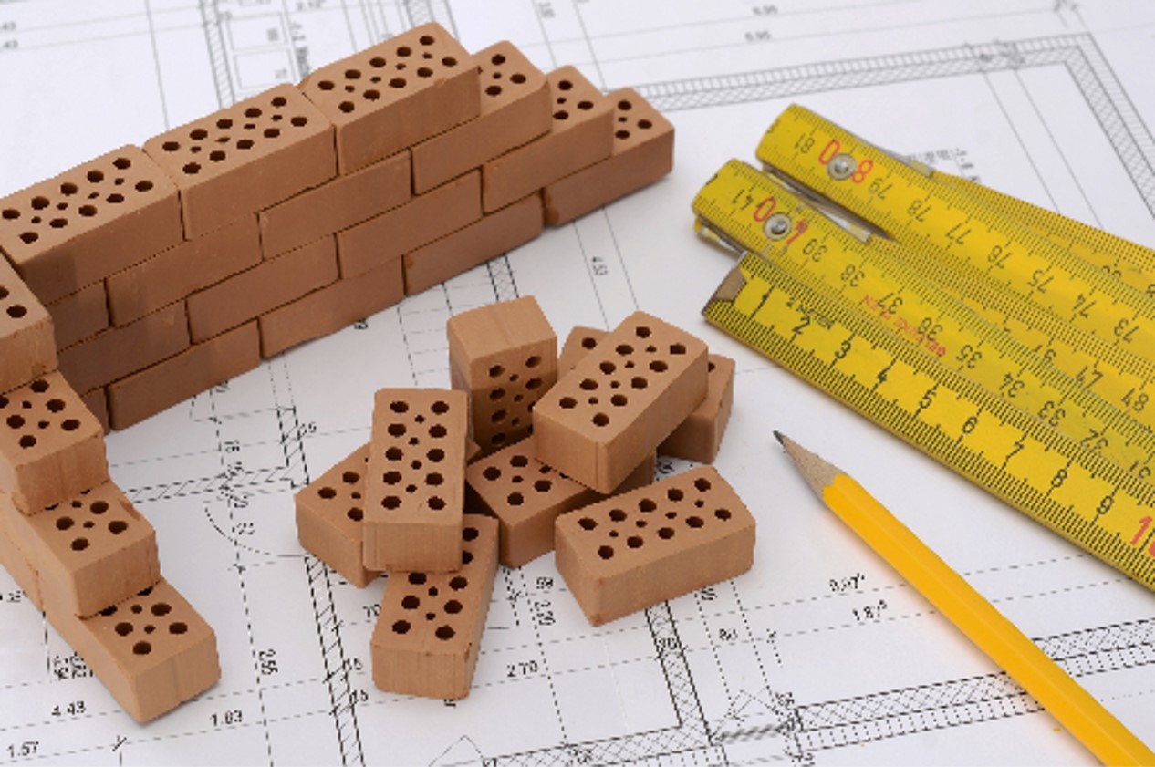 Wooden building blocks, rulers, and a pencil sit on a real estate development plan drawing