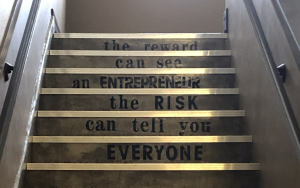 A staircase has the following words stenciled onto its risers: Everyone can tell you the risk. An entrepreneur can see the reward.